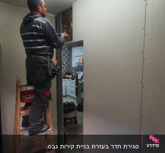 אדם מתקין לוחות גבס על קיר בעזרת כלי עבודה